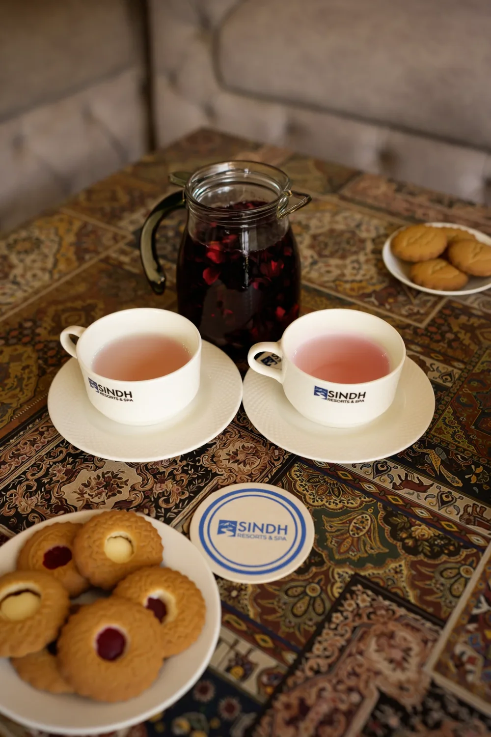 Two cups of herbal tea with a jar of dried petals and a plate of cookies