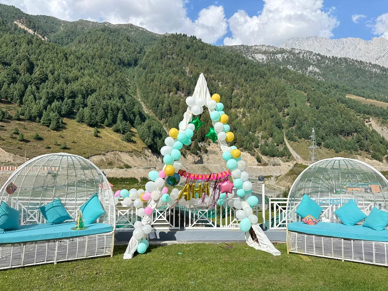 A balloon arch and white lounge domes on the lawn, with forested mountains behind